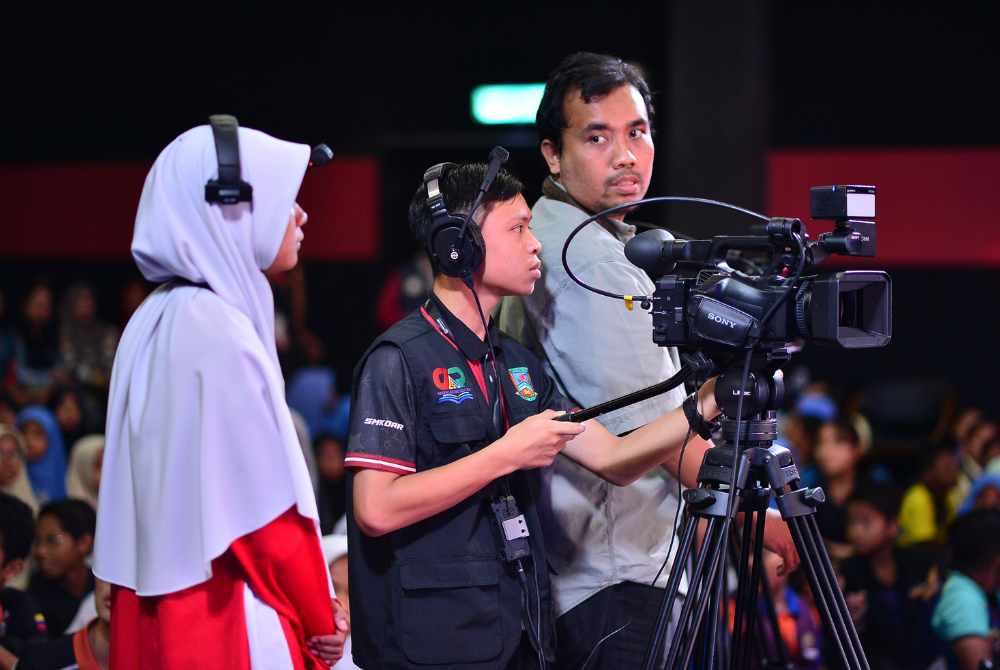 Kru produksi memberi tunjuk ajar kepada peserta yang mempraktikkan kamera untuk siaran langsung audio siar.