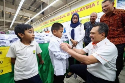 Mohd Izani membantu salah seorang murid mencuba baju sekolah pada program MYAirportCARES Kembali Ke Sekolah bersama Malaysia Airports di sebuah pasaraya. 