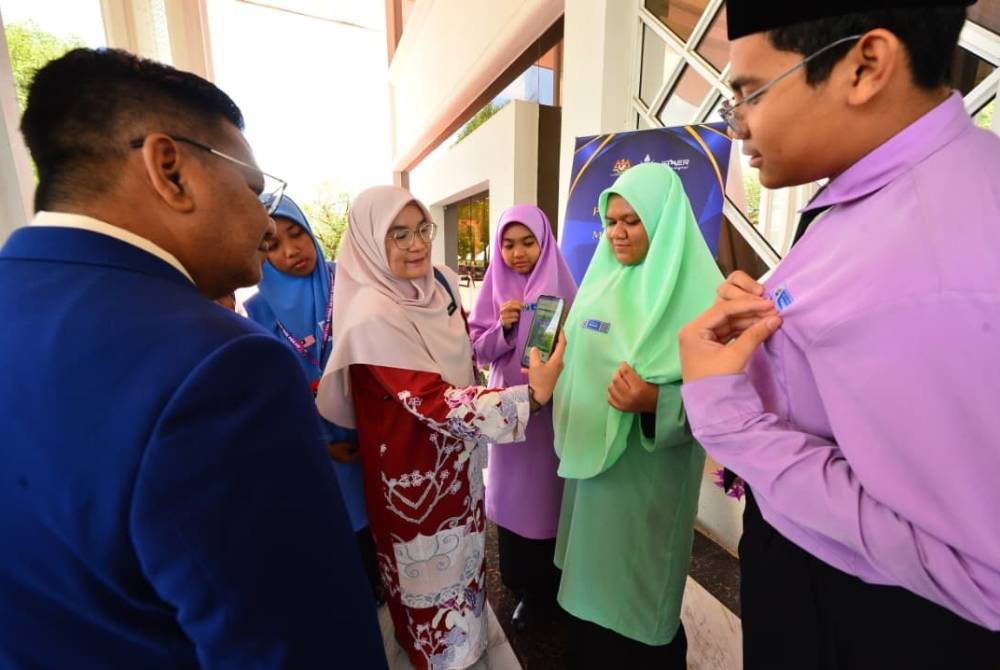 Ab Razif (kiri) melihat guru Sekolah Menengah Kebangsaan Felda Purun, Cikgu Raina Othman (dua kiri) mengimbas kod bar pada lencana yang dipakai oleh pelajar.