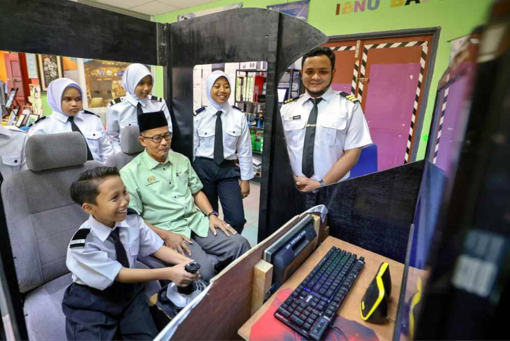 Guru Besar SK Gong Nangka, Azlan Ali (duduk, dua, kiri) dan Tengku Ahmad Fareez (kanan) meninjau latihan simulasi penerbangan oleh murid yang juga ahli kelab itu semasa ditemui, baru-baru ini.