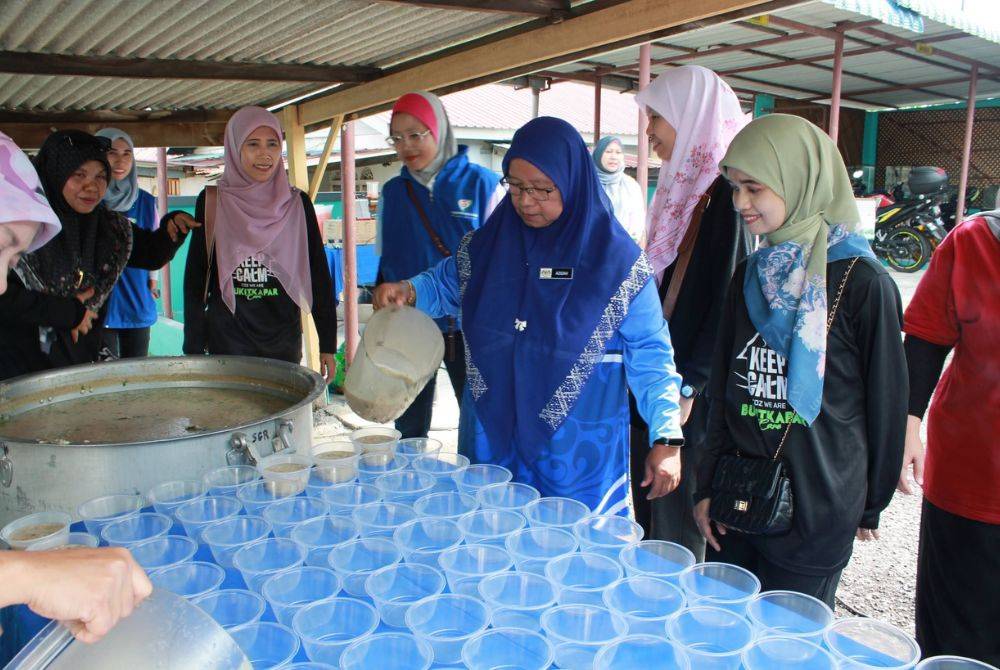 Azizah (dua dari kanan) menuang bubur ke dalam bekas untuk diagihkan kepada semua warga sekolah.