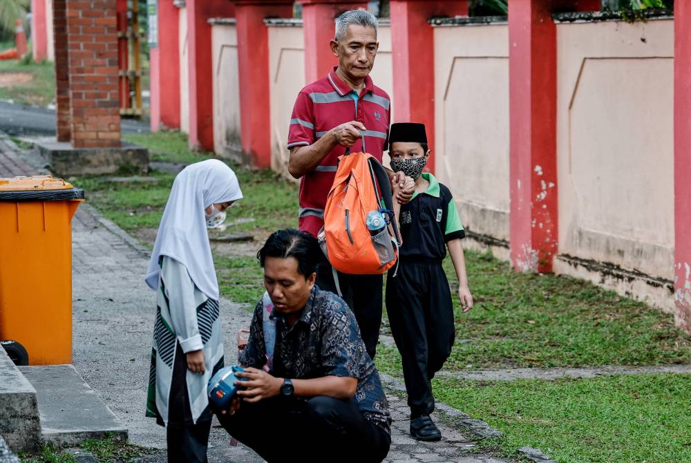 Ibu bapa memastikan anak-anak memakai pelitup muka sebelum memasuki kawasan sekolah. Foto: Bernama
