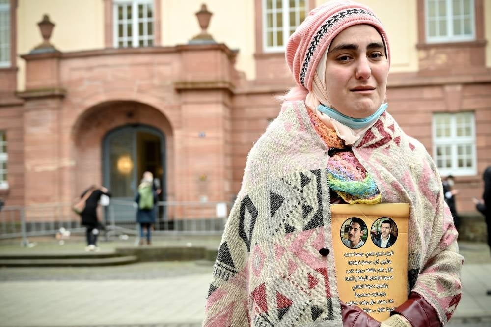 A woman reacts as she shows a picture of her relatives, who died in Syria, after the verdict against a former Syrian secret police officer, at the Higher Regional Court in Koblenz, Germany, Jan 13, 2022. In the world's first trial on Syrian state torture, Anwar Raslan has been sentenced to life imprisonment for crimes against humanity, 27 counts of murder, and other offenses. This was announced by the Higher Regional Court (OLG) in Koblenz. (Source: EPA/SASCHA STEINBACH)