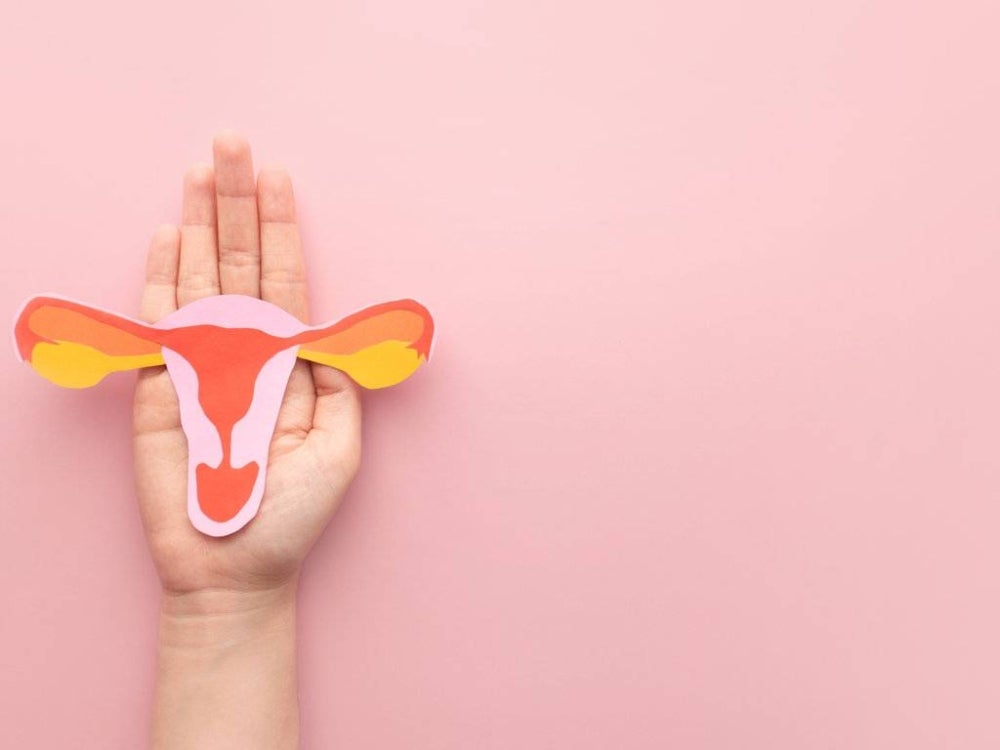 Female reproductive health concept. Woman hand holding uterus shape made frome paper on pink background. Awareness of uterus illness such as endometriosis, PCOS, STDs or gynecologic cancer.