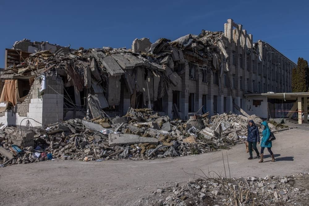 People walk past a severely damaged school after the Russian shelling, in Zhytomyr city, north-west Ukraine on March 20, 2022. - EPA