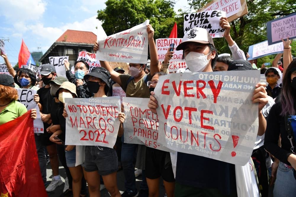 People display placards during a rally in front of the commission on elections in Manila on May 10, 2022, to protest against the results of the May 9 presidential election. (Photo by Ted ALJIBE / AFP)