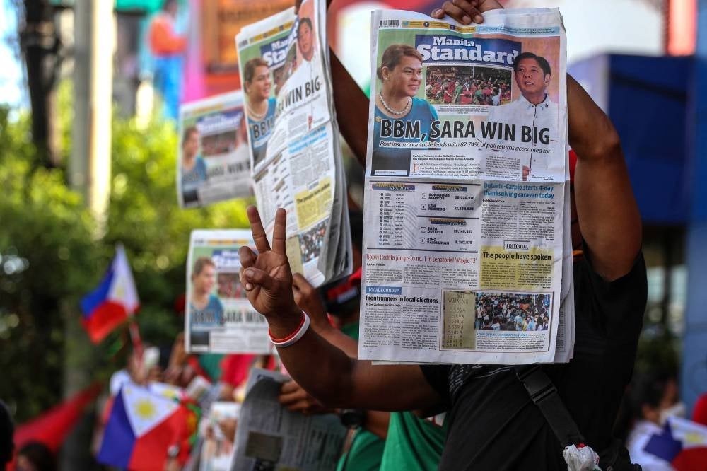 Supporters of Philippine presidential candidate Ferdinand Marcos Jr hold newspapers with coverage of his landslide presidential victory, outside the campaign headquarters in Mandaluyong City, Metro Manila, on May 10, 2022. (Photo by JAM STA ROSA / AFP)