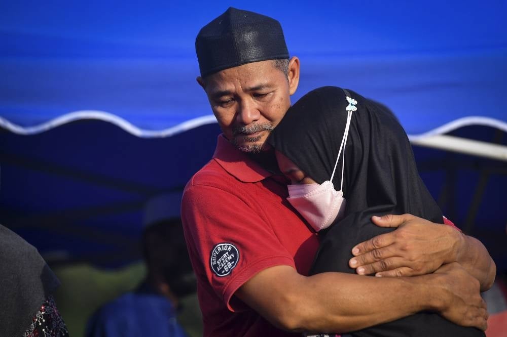 Ahmad Hafizan Abdul Rahman, 49, (left) and his daughter in aguish over the death of his firstborn Ahmad Naim Najmi Ahmad Hafizan, 21, at the Kijal Muslim Cemetery in Chukai, today. - BERNAMA
