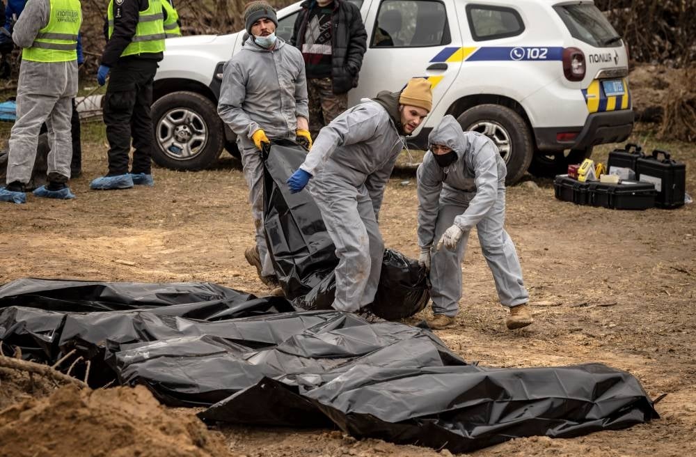 Workers wearing protective gear line up body bags as they exhume bodies at a site where civilians killed during Russian occupation where buried, on the grounds of the Church of Saint Andrew in Bucha, on the outskirts of Kyiv, on April 13, 2022. - AFP