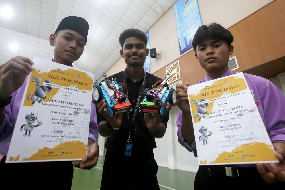 Champions in a robotics competition from SMK (Felda) Seri Sendayan, Putra Danish Haikal Azan Huzzaie (right) and Muhammad Zaim Eddi Hamka (left) with their mentor S.Raxonraj (middle) showing their certificates and robotic model in the competition in conjunction with STEM Day. - BERNAMA