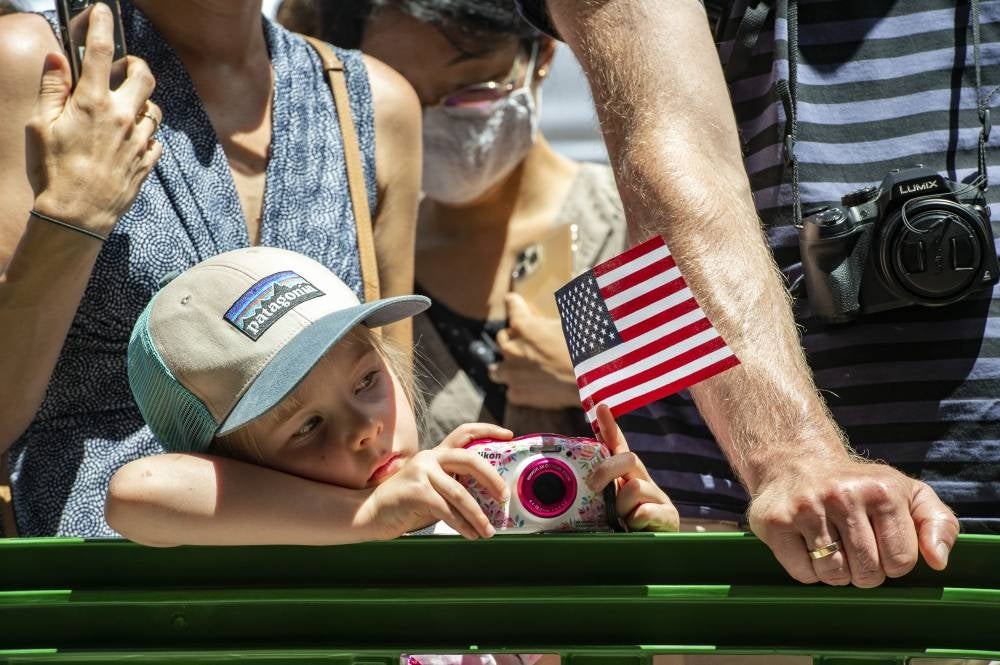 A child holds a US flag and digital camera while waiting for the dogs to walk by during the Patriotic Pooch Parade in Boston, Massachusetts, on July 3, 2022. (Photo by JOSEPH PREZIOSO / AFP)