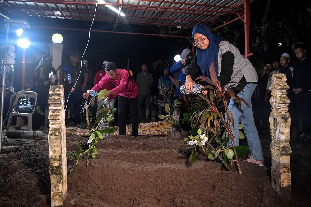 Hazman Rahim and his sister Fatini Rahim at the common grave of the four victims killed in the accident. Photo: BERNAMA