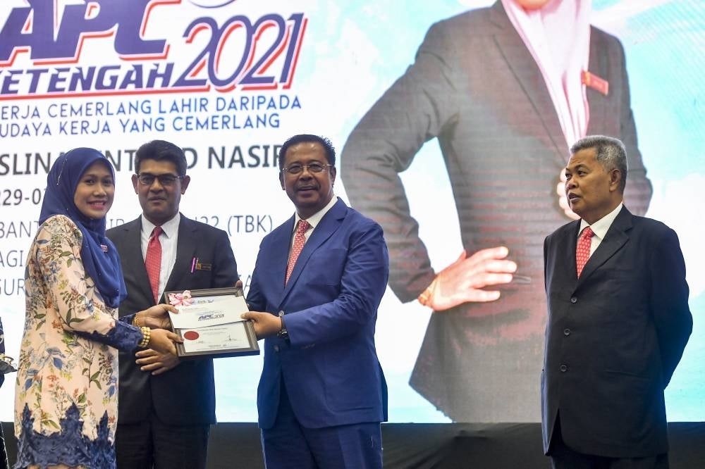 Deputy Rural Development Minister l Datuk Seri Abdul Rahman Mohamad (middle) presenting the Excellent Service Award (APC) to Ketengah employee Roslina Nasir (left) at Bandar Al Muktafi Billah Shah, today. - BERNAMA