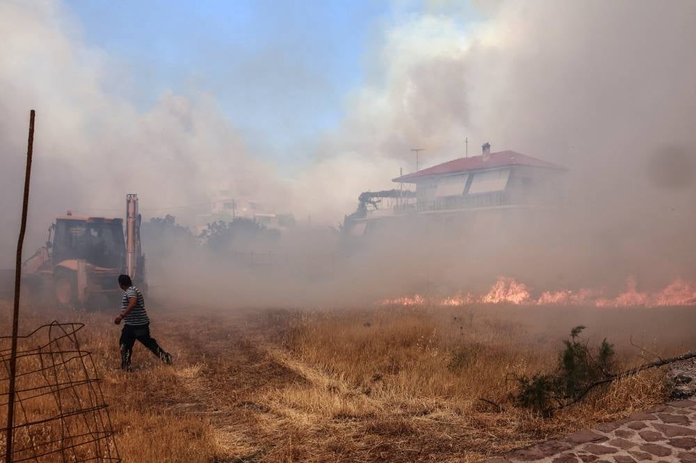 A person runs as wildfire approaches houses on Vatera coastal resort on the eastern island of Lesbos on July 23, 2022. Residents were evacuated as wildfire threatened properties. - (Photo by MANOLIS LAGOUTARIS / AFP)