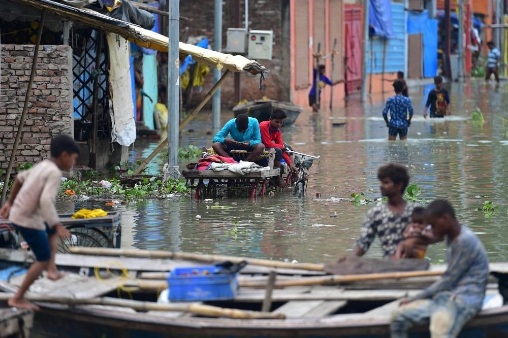 Youths living in a low lying area on the banks of the River Ganges sit on cart in a flooded street at Daraganj area in Allahabad on August 19, 2022, after water levels rose following monsoon rains. (Photo by SANJAY KANOJIA / AFP)