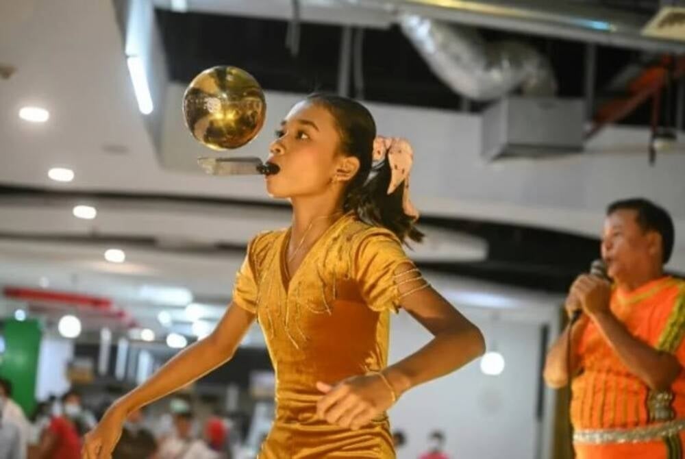 Han Myint Mo keeping up a Myanmar juggling tradition by kicking up a gold-coloured metal ball, pirouettes and catches it on the blade of a knife held in her teeth - AFP Photo