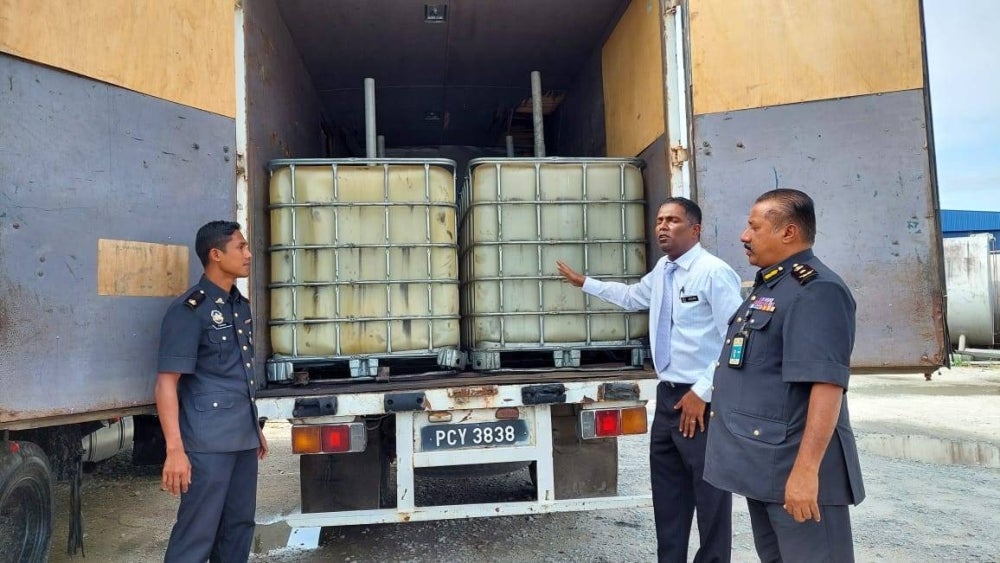 Jegan (two from left) shows an empty plastic bin with a capacity of 1,000 litres that has been modified in the lorry. - Photo: Penang KPDNHEP
