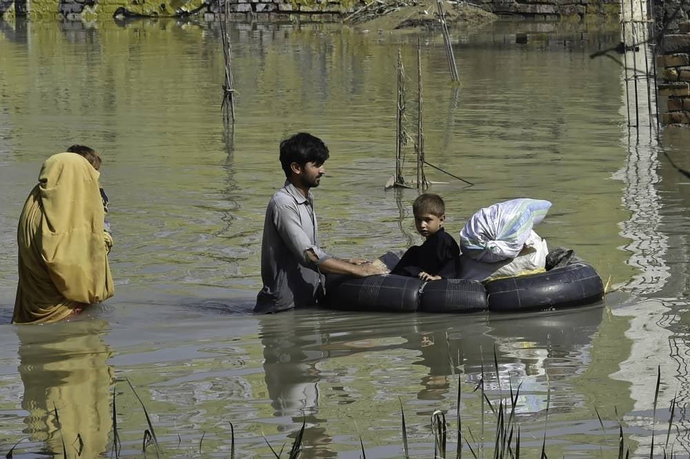 A family wades through a flood hit area following heavy monsoon rains in Charsadda district of Khyber Pakhtunkhwa on Aug 29, 2022. - (Photo by ABDUL MAJEED / AFP)