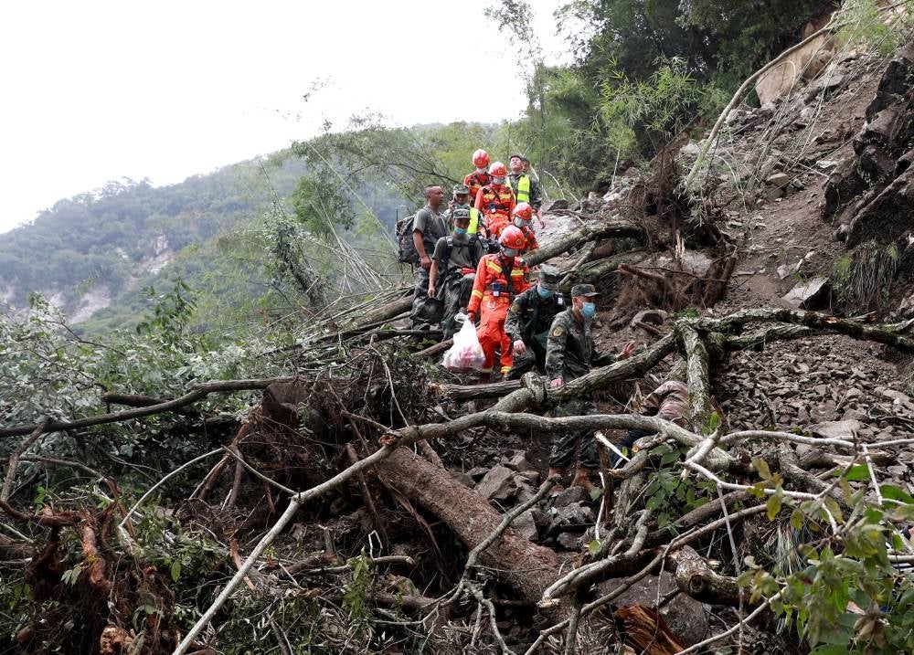 This photo taken on Sept 6, 2022 shows rescuers walking past uprooted trees from a landslide as they head to an earthquake-affected area following a 6.6-magnitude earthquake that struck on Sept 5, in Shimian county, Ya'an city, in China's southwestern Sichuan province. (Photo by CNS / AFP)