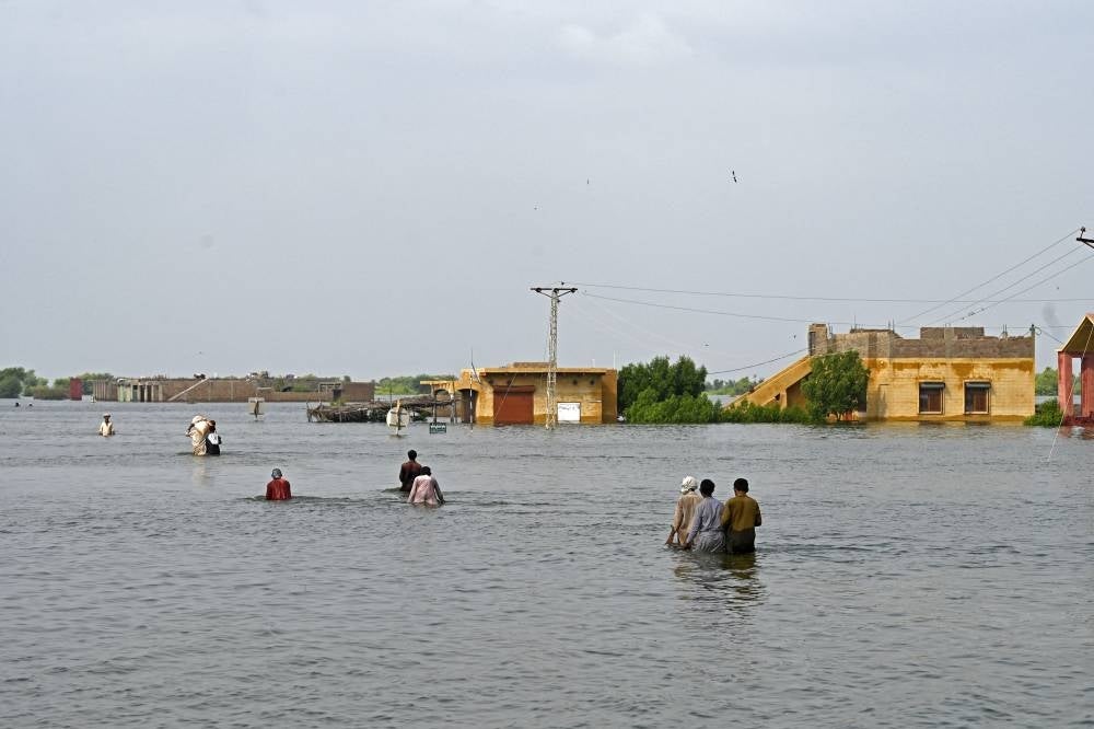 Internally displaced people wade through floodwaters to return home after heavy monsoon rains in Dadu district, Sindh province on Sept 7, 2022. (Photo by Aamir QURESHI / AFP)