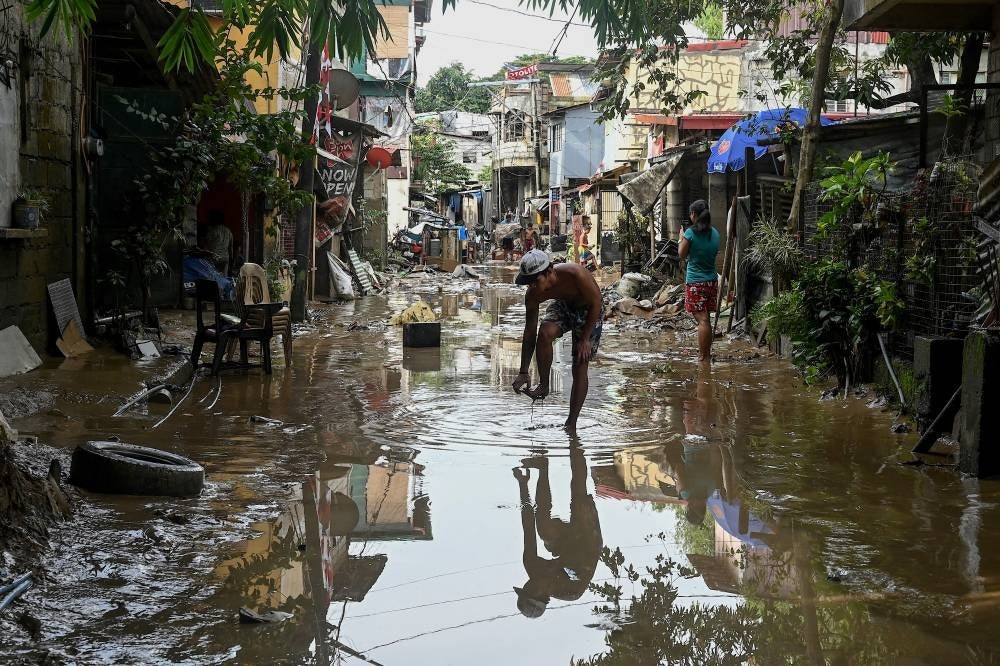 A man adjusts his shoe while walking through a flooded area in the aftermath of Super Typhoon Noru in San Mateo, Rizal province on Sept 26, 2022. (Photo by JAM STA ROSA / AFP)