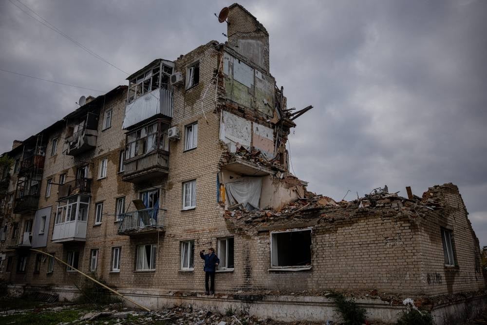 A man takes pictures with a phone beside a damaged building in Lyman, Donetsk region, on Oct 21, 2022, after the recapture of the area from the Russian forces, amid the Russian invasion of Ukraine. - (Photo by DIMITAR DILKOFF / AFP)