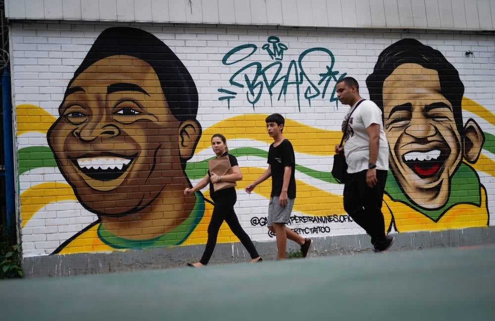 People walk by a mural depicting Brazil's late football players Pele (L) and Garrincha (R) at Tijuca neighbourhood in Rio de Janeiro, Brazil, on December 29, 2022, just hours after the passing of Pele at a Sao Paulo hospital. Pic by Mauro Pimentel/ AFP)