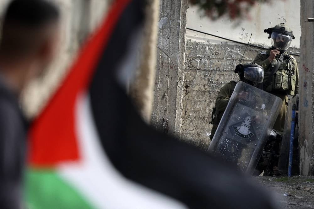 A Palestinian demonstrator waves a national flag during confrontations with Israeli troops, following a protest against the expropriation of Palestinian land by Israel in the occupied - West Bank, in the village of Kfar Qaddum, near the Jewish settlement of Kedumim on Jan 6, 2023. - (Photo by JAAFAR ASHTIYEH / AFP)