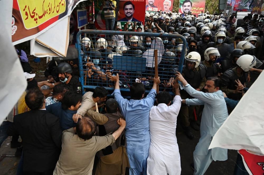 Supporters (foreground) of former prime minister Imran Khan and riot police scuffle outside Khan's house to prevent officers from arresting him, in Lahore on March 14, 2023. - (Photo by ARIF ALI / AFP)