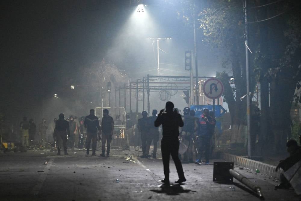 Police personnel and supporters of former Pakistan prime minister Imran Khan gather along a street near Khan's residence, in Lahore on March 15, 2023. - (Photo by ARIF ALI / AFP)