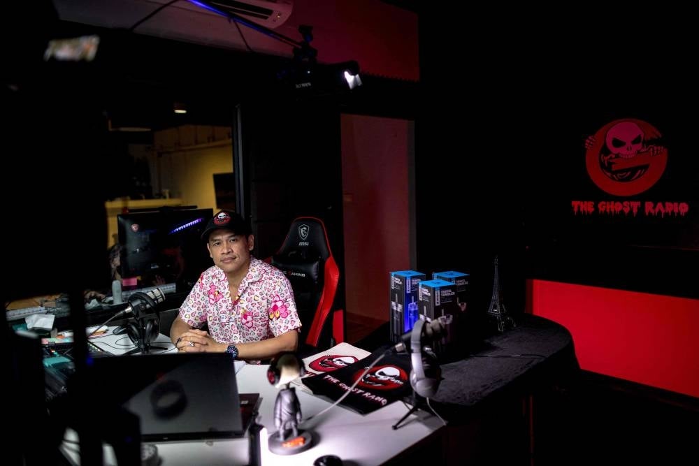 Ghost Radio station host Jack Watcharaphon poses in his studio in Bangkok. - It is almost midnight, and above a semi-abandoned Bangkok shopping centre, Ghost Radio is on air. Rapid-fire comments ping across the studio's screens as thousands tune in online to hear callers describe their encounters with Thailand's supernatural. - Pic: AFP