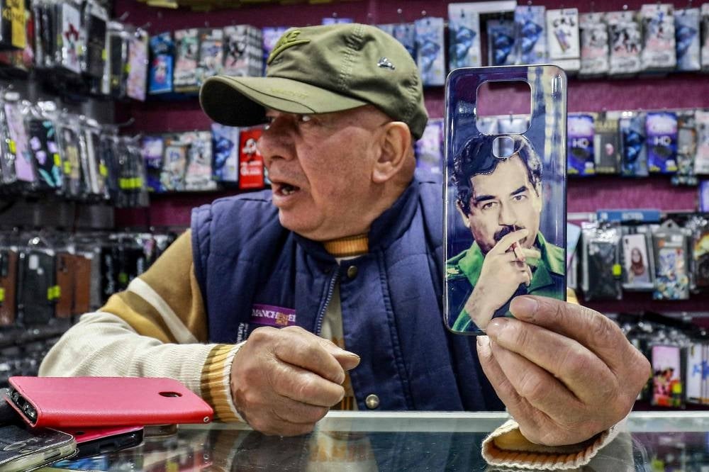 Shaher Abu Sharkh, a 67-year-old Jordanian mobile phone accessory merchant holds up a cell phone cover showing the image of Iraq's late ousted dictator Saddam Hussein in his shop in Amman. - Twenty years after the fall of his regime, the late Iraqi president Saddam Hussein remains admired and popular in Jordan where his image can still be seen across the country. The instantly recognisable face peers out from car stickers to mobile phone covers in Jordan, despite symbols and images associated with his rule being widely considered taboo in Iraq itself. - Pic: AFP