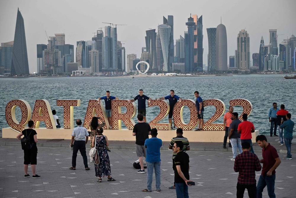  In this file photo taken on December 03, 2022 People pose for photos at the Corniche promenade as Doha's skyline is seen in the background during the Qatar 2022 World Cup football tournament. - Months after hundreds of thousands of football fans packed into its hotels and stadiums, Qatar is seeking to remedy a bout of the post-World Cup blues by hosting more international events. Along with the departed football crowds, thousands of foreign workers left the Gulf state after Lionel Messi lifted the coveted trophy on December 18. Many of those who stayed on are counting the cost. - Pic: AFP