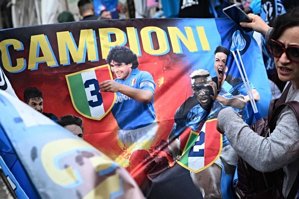 A woman looks at a Napoli flag in a street stall in Toledo street in central Naples on April 29, 2023, on the eve of the Italian Serie A football match between Napoli and Salernitana. - Naples, as the city braces up for its potential first Scudetto championship win in 33 years. An incredible 19 points clear at the top of Serie A, it's surely only a matter of time until southern Italy's biggest club win the Scudetto for the first time since 1990, when Diego Maradona was still strutting his stuff in sight of Mount Vesuvius. - Pic: AFP