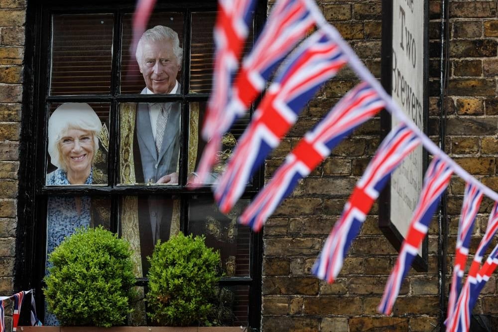 Cardboards picturing Britain's Camilla, Queen Consort (L) and Britain's King Charles III are displayed on the window of a pub in a street adorn with Union Jack flags, in Windsor, on May 2, 2023, ahead of the coronation ceremony of Charles III and his wife, Camilla, as King and Queen of the United Kingdom and Commonwealth Realm nations, on May 6, 2023 - AFP 