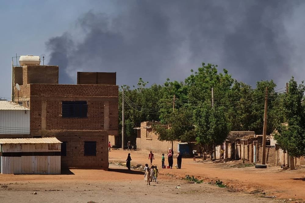 People walk as smoke billows in the background during fighting in the Sudanese capital Khartoum, on May 3, 2023. - AFP