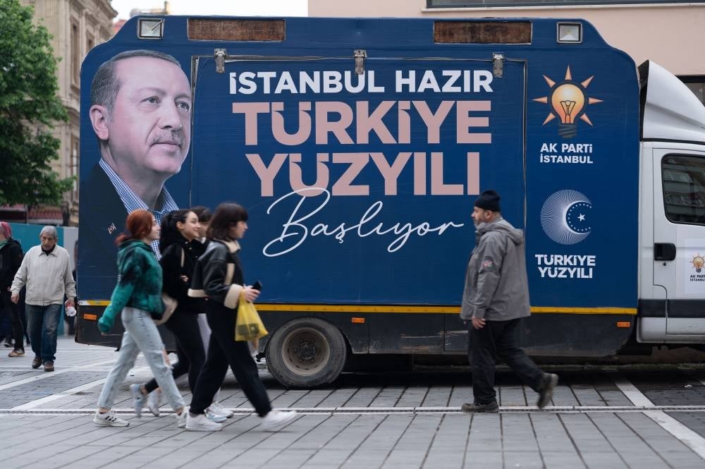 Youths walk by a presidential election truck depicting Turkish president Recep Tayyip Erdogan in the Kasimpasa district of Istanbul, the president's childhood neighbourhood known as the “castle of Erdogan”, on April 20, 2023, ahead of Turkey's presidential elections on May 14th. (Photo by Eylul YASAR / AFP)