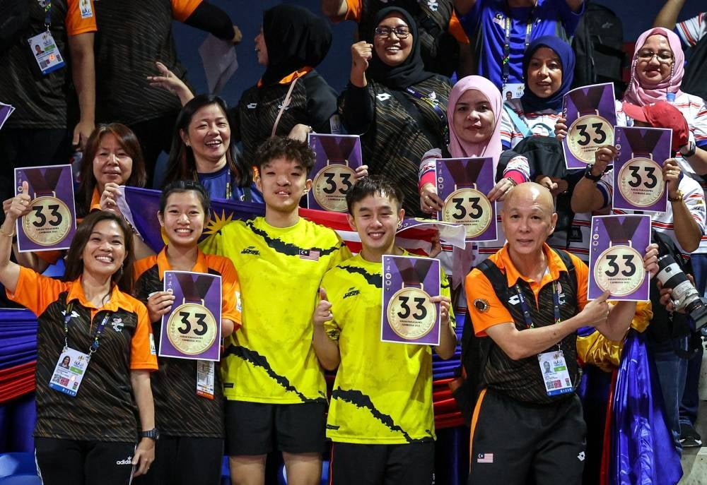 Malaysian supporters holding '33 golds' poster afterChee Chaoming-Brady Chin clinch the 33rd gold medal through the men’s doubles table tennis competition at Morodok Techo Stadium last night.
