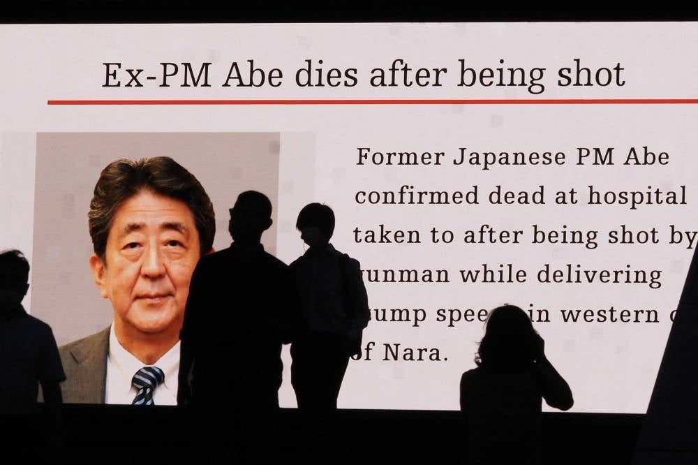 (FILES) Pedestrians are silhouetted against a large public video screen showing an image of former Japanese prime minister Shinzo Abe in the Akihabara district of Tokyo on July 8, 2022, after he was shot and killed in the city of Nara. - AFP