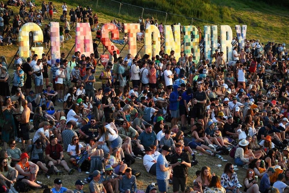 (FILES) Festivalgoers attend the Glastonbury festival near the village of Pilton in Somerset, southwest England, on June 22, 2022. The iconic Glastonbury Festival opens its doors on Wednesday, with 200,000 music fans set to descend on a farm in southwest England to see acts including Arctic Monkeys, Guns N'Roses and Elton John. While able to draw the biggest performers from every genre and generation, the long-running festival is equally known for hosting thousands of small acts and for the leftfield events across its huge site. (Photo by Andy Buchanan / AFP)