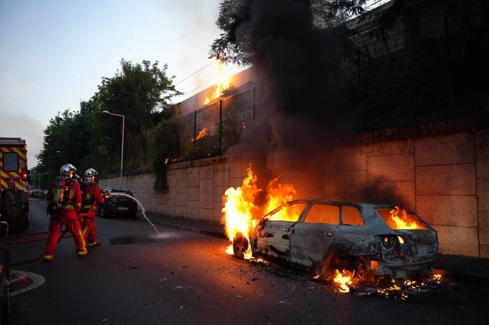 Firefighters work to put out a fire next to a burning car on the sidelines of a demonstration in Nanterre, west of Paris, on June 27, 2023, after French police killed a teenager who refused to stop for a traffic check in the city. Photo by Zakaria Abdelkafi/AFP