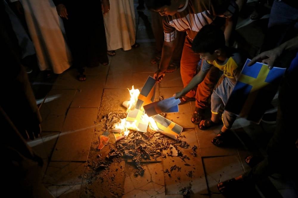Supporters of Iraqi Shiite cleric Moqtada Sadr burn posters depicting the Swedish flag during a protest in Karbala on June 29, 2023, denouncing the burning of the Koran in Sweden. Photo by Mohammed Sawaf/AFP