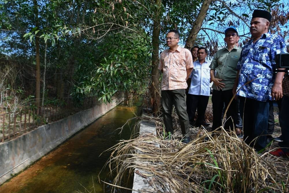 Natural Resources, Environment and Climate Change Minister Nik Nazmi Nik Ahmad (left) observing one of the projects to build and upgrade the irrigation system in Taman Wadi Iman, in Kok Lanas, today - Photo by Bernama