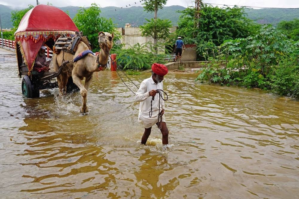A man with his camel wade across a flooded street after heavy monsoon rains in Pushkar, in India's Rajasthan state on July 10, 2023. - (Photo by HIMANSHU SHARMA / AFP)