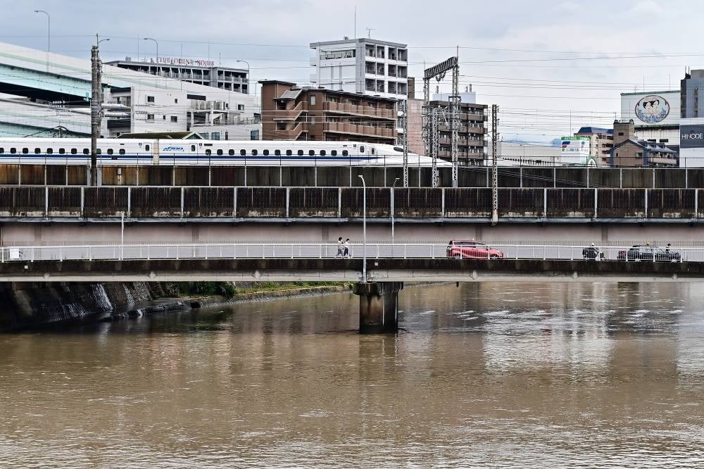 A Japanese Shinkansen high-speed train passes by as pedestrians cross a bridge over the Mikasa river in Fukuoka city on July 10, 2023. - (Photo by MANAN VATSYAYANA / AFP)