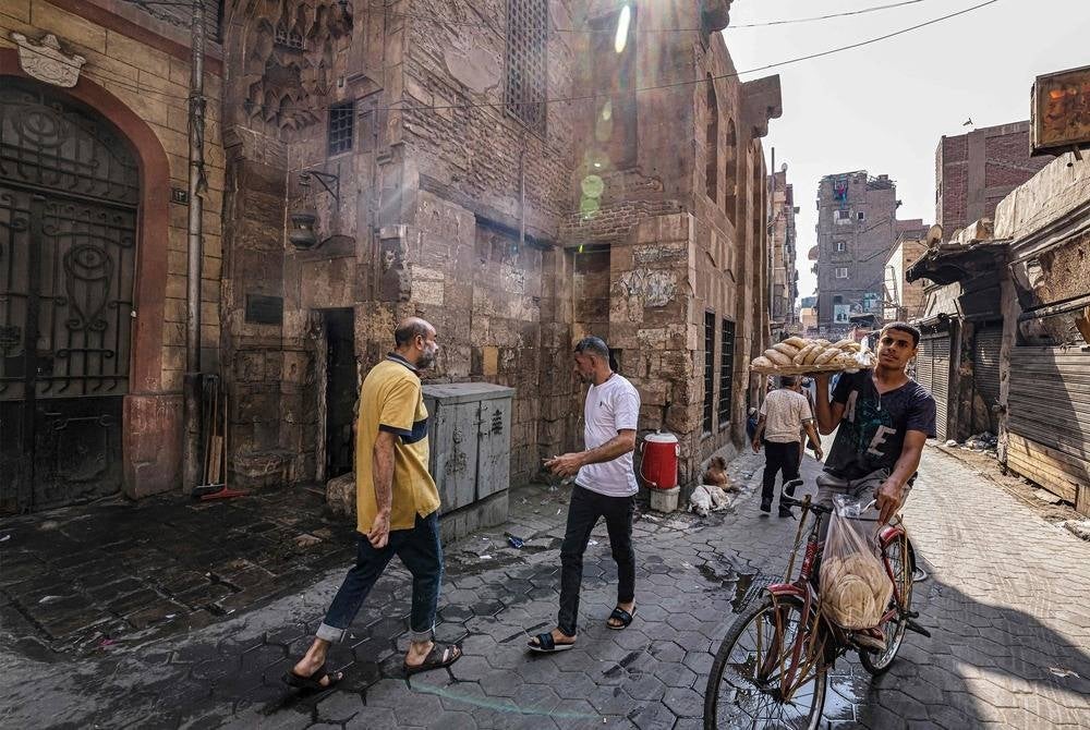 A deliveryman riding a bicycle carries a tray of fresh traditional Egyptian bread on his arm from a bakery along an alley in the Darb el-Ahmar district of Cairo on July 27, 2023. (Photo by Khaled DESOUKI / AFP)