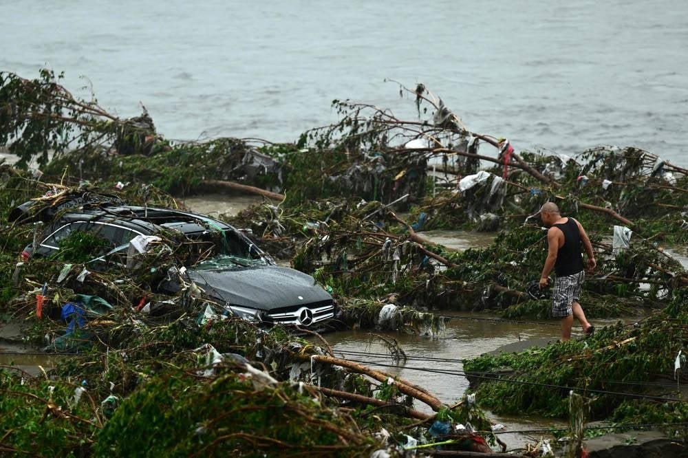 A man looks at a damaged car following heavy rains in Fangshan district in Beijing on August 1, 2023. At least 11 people were killed and 13 were missing after heavy rains lashed Beijing, state media said on August 1, in downpours that have submerged roads and deluged neighbourhoods with mud. (Photo by Pedro PARDO / AFP)