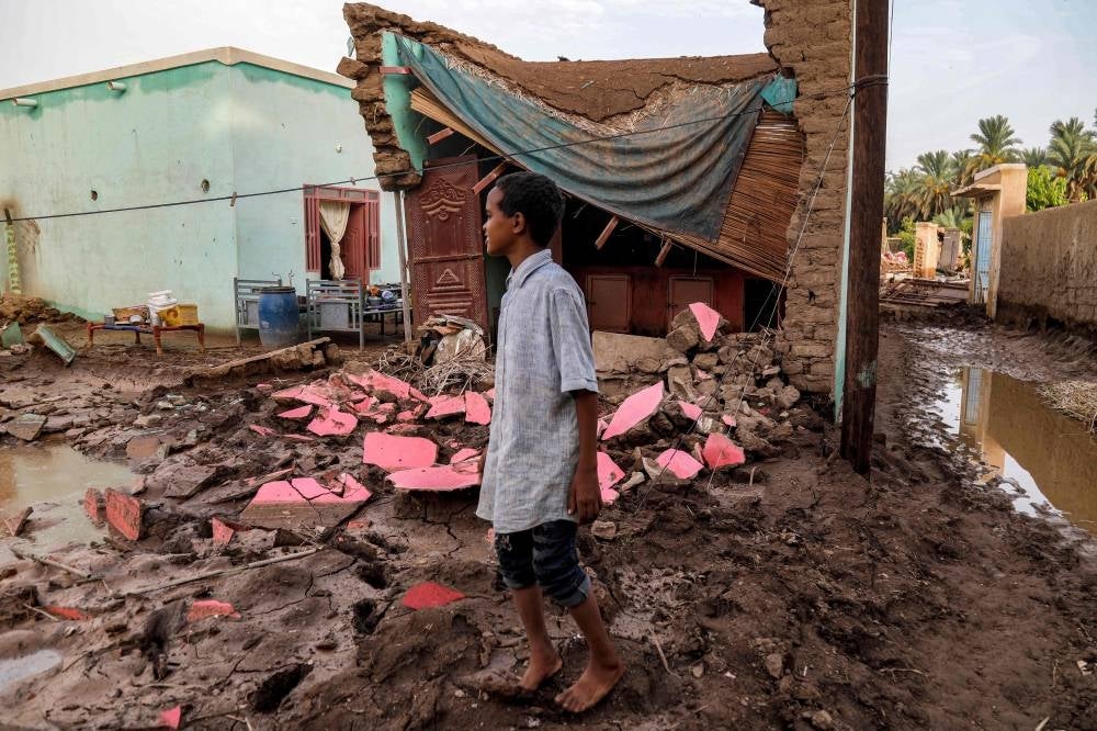 A boy stands by a destroyed house in the aftermath of a flood in al-Sagai north of Omdurman in war torn Sudan - AFP 