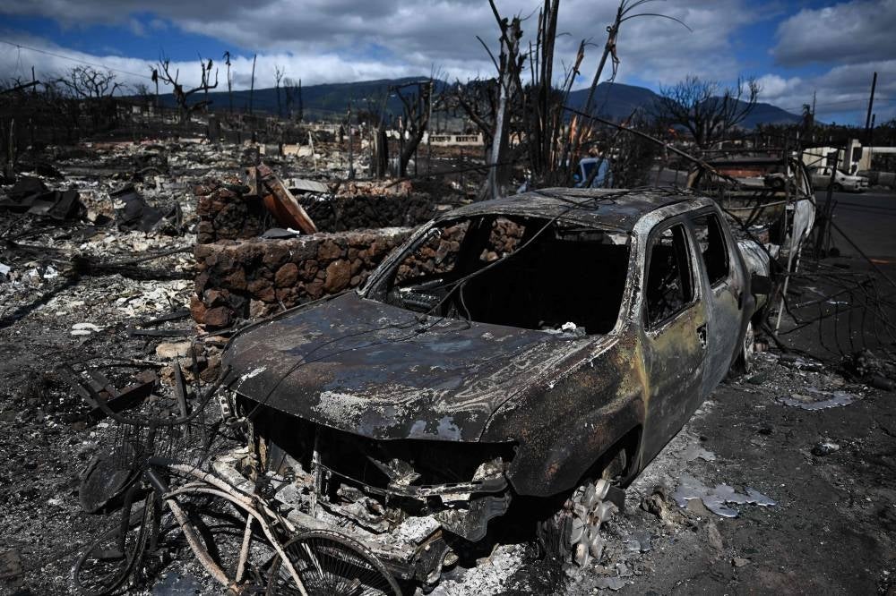 A burnt-out car lies in the driveway of a charred house in the aftermath of a wildfire in Lahaina, western Maui, Hawaii on August 11, 2023. A wildfire that left Lahaina in charred ruins has killed at least 67 people, authorities said on August 11, making it one of the deadliest disasters in the US state's history. Brushfires on Maui, fueled by high winds from Hurricane Dora passing to the south of Hawaii, broke out August 8 and rapidly engulfed Lahaina. (Photo by Patrick T. Fallon / AFP)