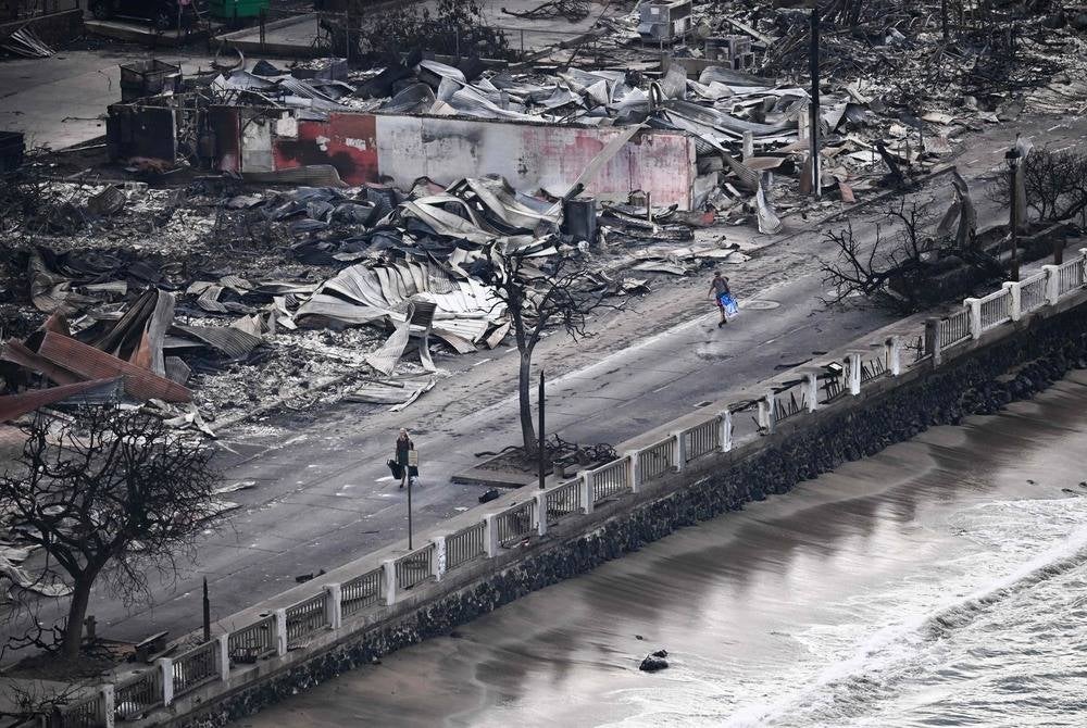 An aerial image taken on Aug 10, 2023 shows a person walking down Front Street past destroyed buildings burned to the ground in Lahaina in the aftermath of wildfires in western Maui, Hawaii. (Photo by Patrick T. Fallon / AFP)